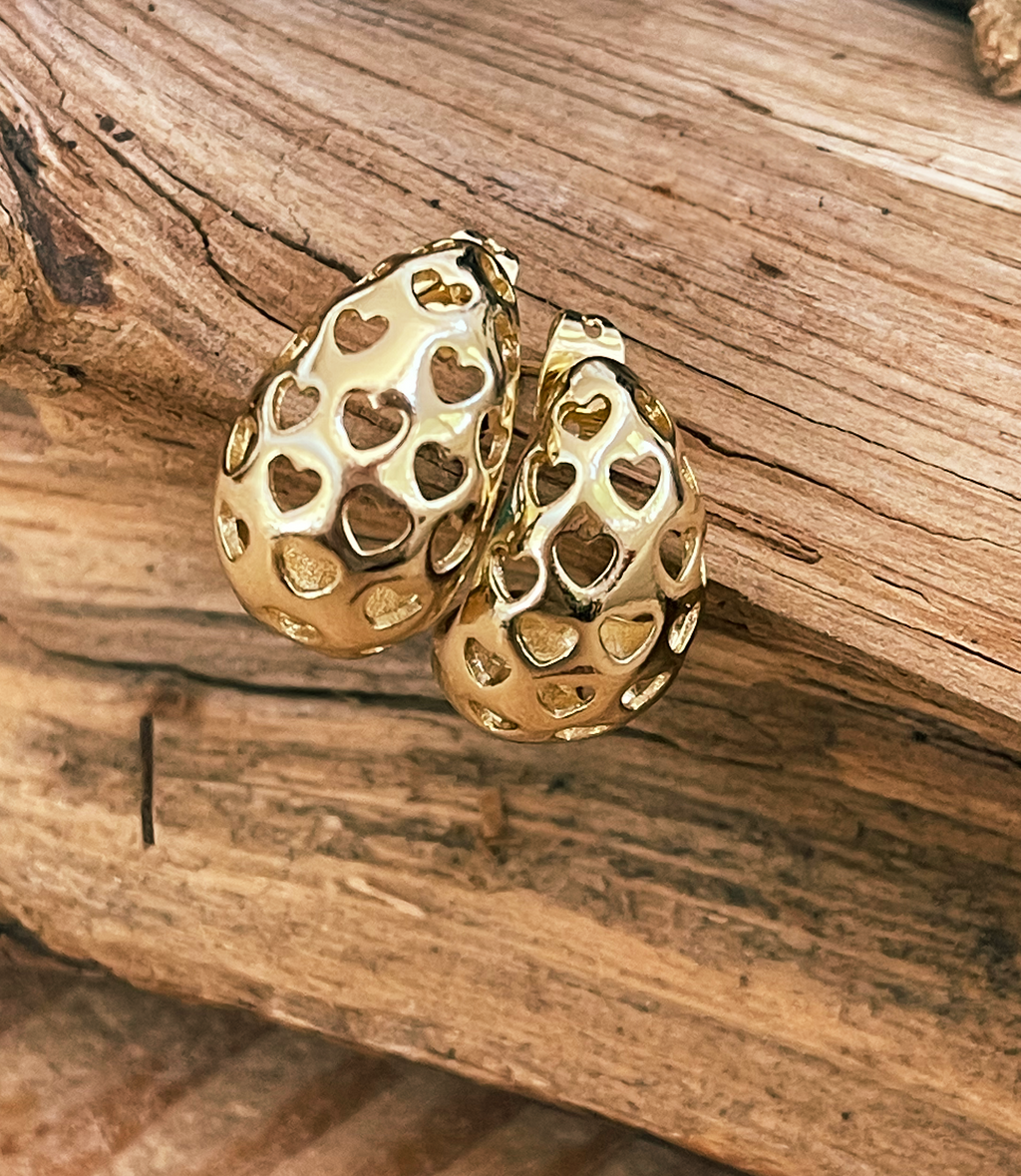 Gold hoop earrings with heart patterns on a wooden surface