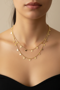 Close-up of a person wearing a gold necklace with heart-shaped pendants on a neutral background