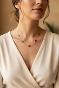 Woman wearing a delicate necklace with red floral pendants against a neutral background