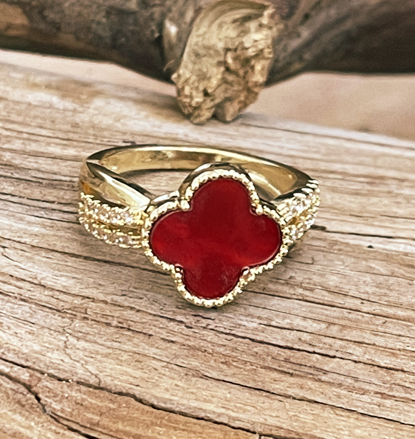 Gold ring with a red clover-shaped stone on a wooden surface