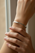 Close-up of a hand wearing a silver bracelet with engraved text, holding another hand.