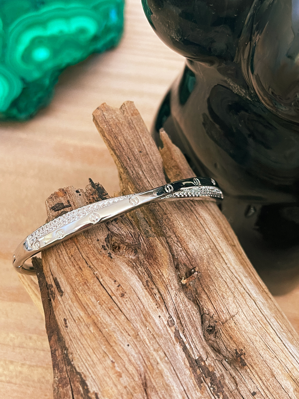 Silver bracelet on a wooden surface with a green stone in the background