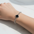 Silver bracelet with a black clover-shaped charm on a wrist against a white background